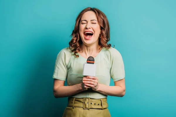 Fröhlicher Journalist lacht, während er das Mikrofon auf blauem Hintergrund hält — Stockfoto