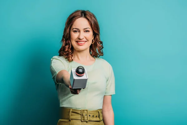 Jornalista positivo sorrindo para a câmera enquanto segurava o microfone no fundo azul — Fotografia de Stock