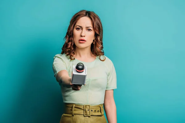 Periodista serio mirando a la cámara mientras sostiene el micrófono sobre fondo azul - foto de stock