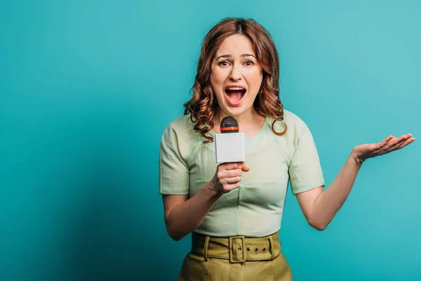 Angry journalist standing with open arm while screaming in microphone on blue background — Stock Photo