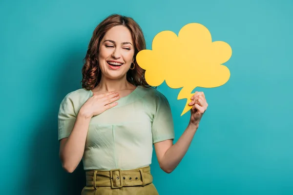 Smiling woman holding hand on chest while holding thought bubble on blue background — Stock Photo