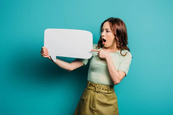 Mujer conmocionada señalando con el dedo a la burbuja del habla sobre fondo azul — Stock Photo