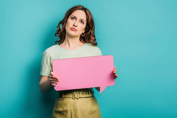 Nachdenkliche Frau blickt auf, während sie eine Sprechblase auf blauem Hintergrund hält — Stockfoto