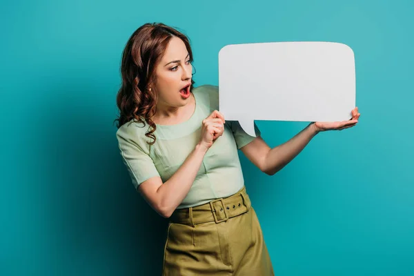 Chica impactada mirando la burbuja del habla sobre fondo azul - foto de stock