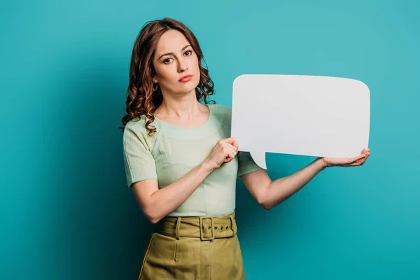 Serious girl looking at camera while holding speech bubble on blue background — Stock Photo