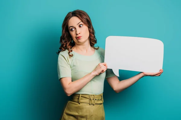 Skeptical girl grimacing while holding speech bubble on blue background — Stock Photo