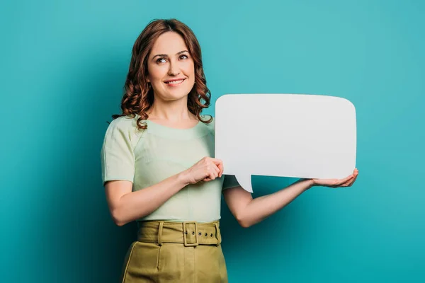 Positive girl looking away while holding speech bubble on blue background — Stock Photo