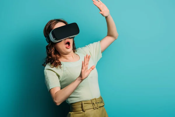 Shocked girl in vr headset gesturing on blue background — Stock Photo