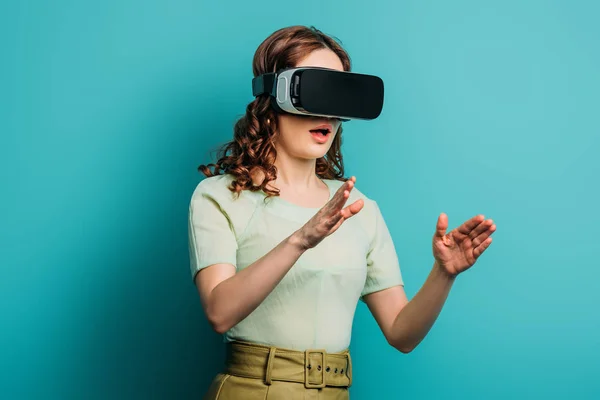 Surprised girl in vr headset gesturing on blue background — Stock Photo