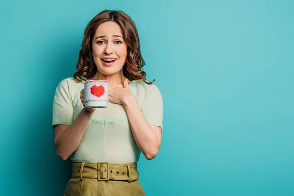 Fille excitée tenant tasse avec symbole de coeur sur fond bleu — Photo de stock