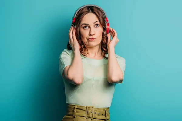 Skeptical girl in wireless headphones looking up on blue background — Stock Photo