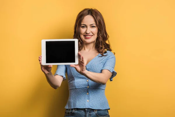 Улыбающаяся женщина показывает цифровой планшет с чистым экраном на желтом фоне — стоковое фото
