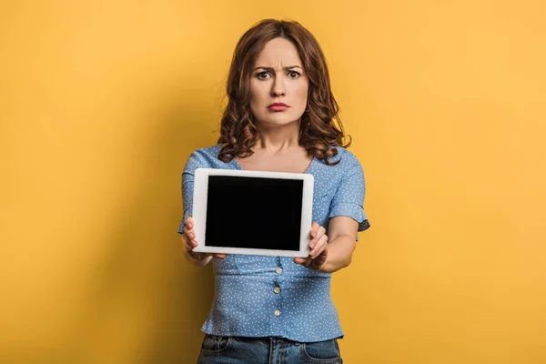 Mulher irritada mostrando tablet digital com tela em branco no fundo amarelo — Fotografia de Stock