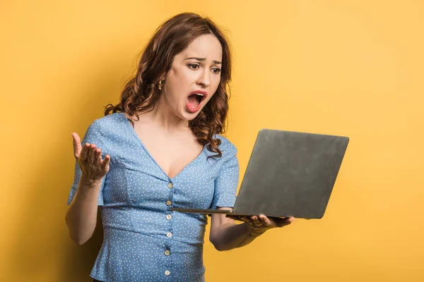 Angry woman screaming during video chat on laptop on yellow background — Stock Photo