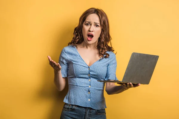 Раздраженная женщина кричит, держа ноутбук на желтом фоне — стоковое фото
