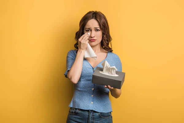 Menina chateada cobrindo lágrimas com guardanapo de papel no fundo amarelo — Fotografia de Stock