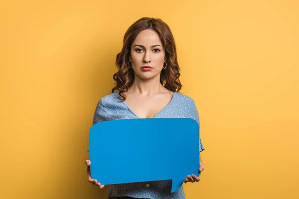 Serious girl looking at camera while holding speech bubble on yellow background — Stock Photo