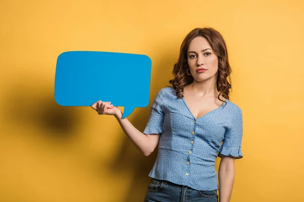 Offended girl looking at camera while holding speech bubble on yellow background — Stock Photo