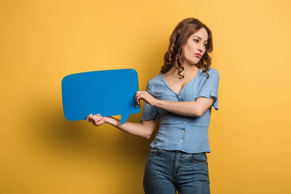 Offended girl looking away while holding speech bubble on yellow background — Stock Photo