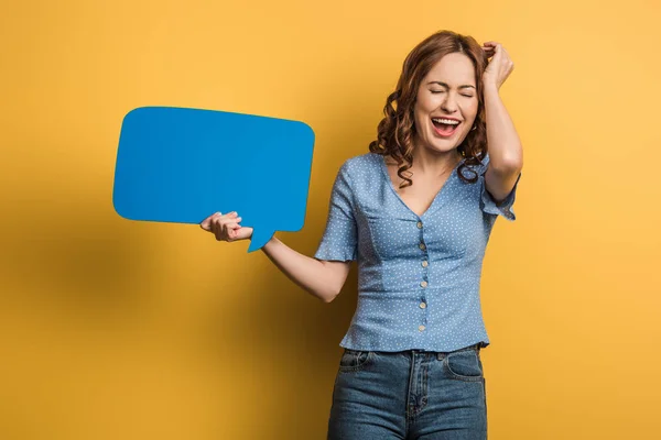 Cheerful woman laughing with closed eyes while holding speech bubble on yellow background — Stock Photo