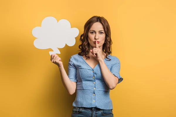 Positive junge Frau zeigt Schweigezeichen, während sie Gedankenblase auf gelbem Hintergrund hält — Stockfoto