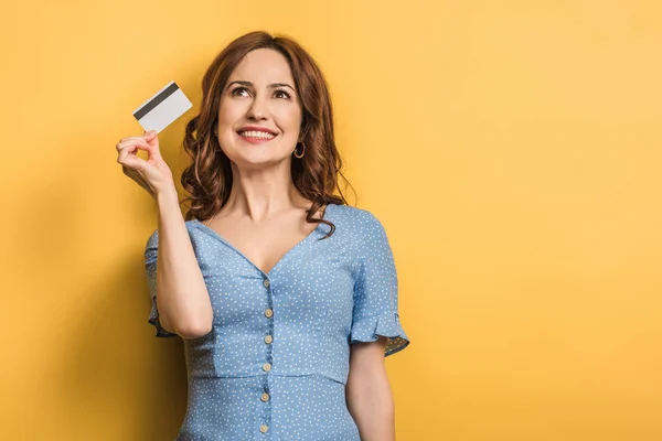 Happy young woman holding credit card on yellow background — Stock Photo