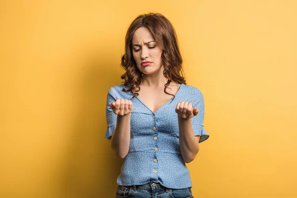 Upset young woman looking at manicure on yellow background — Stock Photo