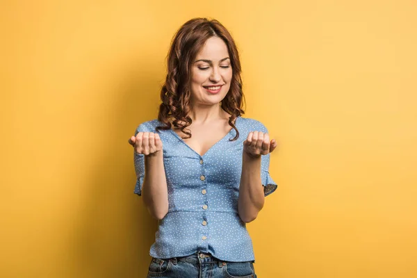 Heureuse jeune femme regardant manucure sur fond jaune — Photo de stock