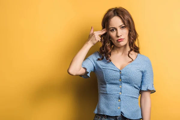 Upset woman imitating self-killing while showing shooting gesture on yellow background — Stock Photo