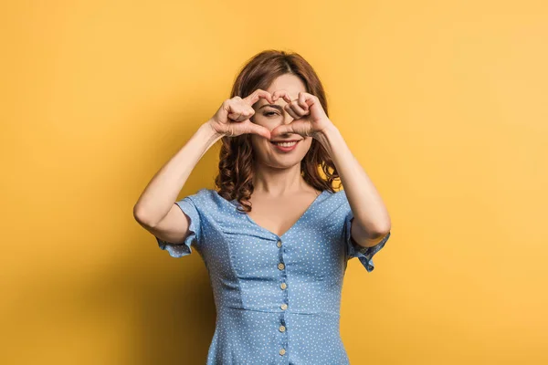 Cheerful girl showing heart with hands on yellow background — Stock Photo