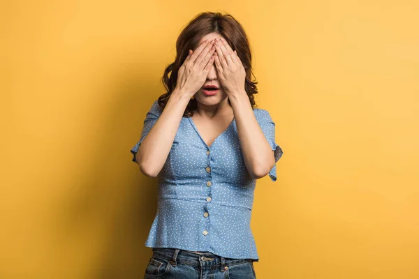 Schockiertes Mädchen, das Augen mit Händen auf gelbem Hintergrund bedeckt — Stockfoto