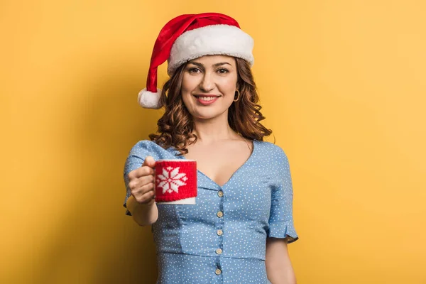 Feliz chica en santa hat celebración taza de bebida caliente sobre fondo amarillo - foto de stock