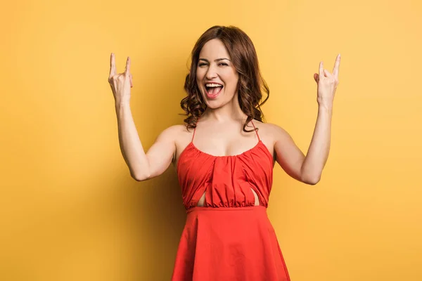Cheerful girl showing rock sings and laughing at camera on yellow background — Stock Photo