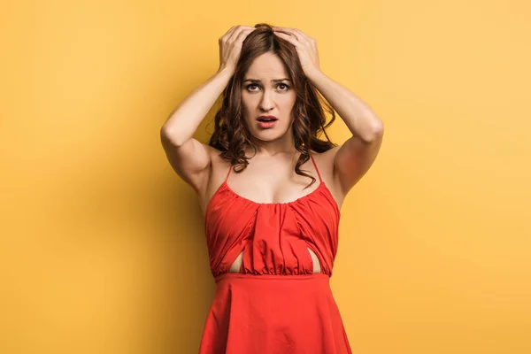 Unzufriedene junge Frau hält Hände auf dem Kopf auf gelbem Hintergrund — Stockfoto