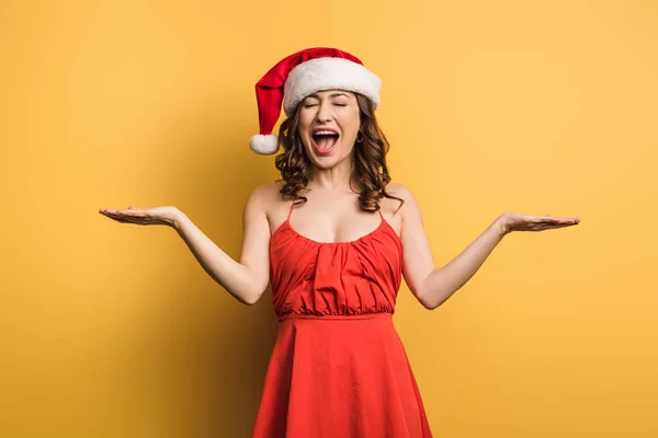 Щаслива дівчина в капелюсі Санта сміється з відкритими руками на жовтому фоні — стокове фото