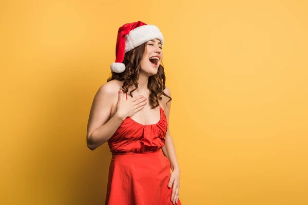 Весела дівчина в капелюсі Санта сміється з закритими очима на жовтому фоні — стокове фото