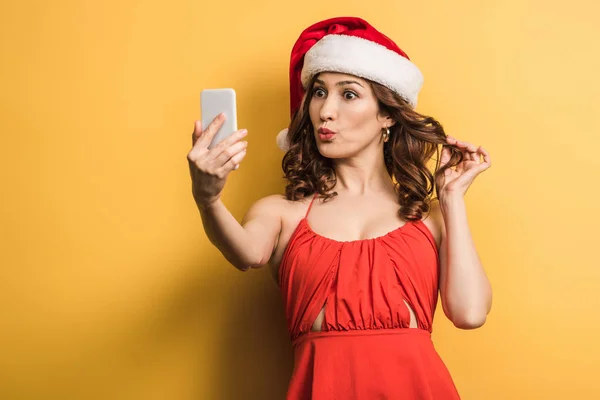 Tricky girl with duck face taking selfie on smartphone on yellow background — Stock Photo