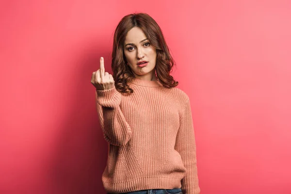 Displeased girl looking at camera and showing middle finger on pink background — Stock Photo