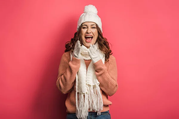 Gaie fille en chapeau chaud et écharpe riant à la caméra sur fond rose — Photo de stock