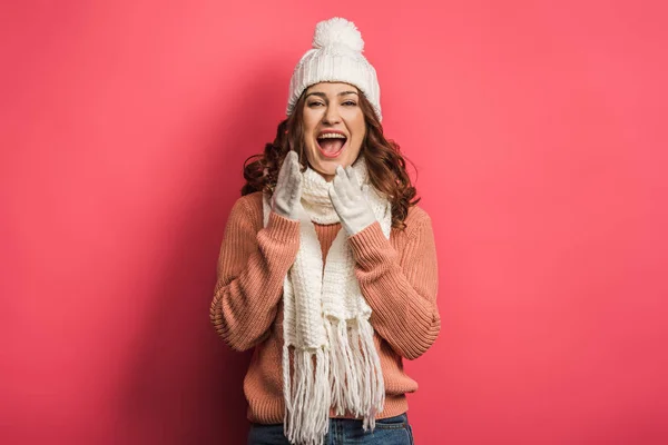 Menina alegre em chapéu quente e cachecol rindo da câmera no fundo rosa — Fotografia de Stock