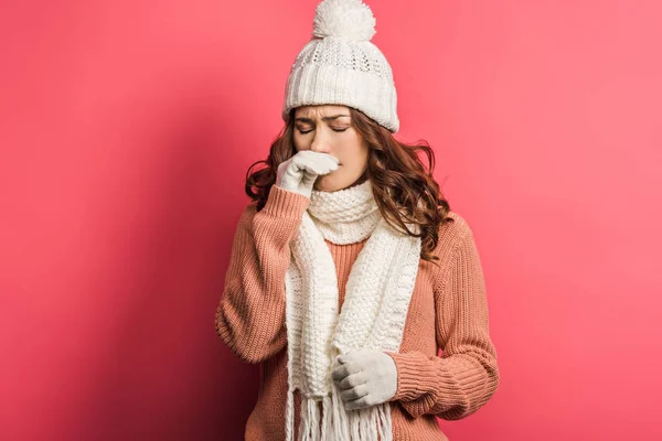 Fille malade en chapeau chaud et écharpe toucher le nez sur fond rose — Photo de stock