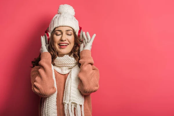 Felice ragazza ascoltando musica in cuffie senza fili con gli occhi chiusi su sfondo rosa — Foto stock