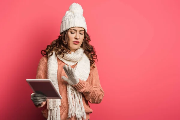 Ragazza scontento in caldo cappello e sciarpa tenendo tablet digitale e mostrando gesto stop su sfondo rosa — Foto stock