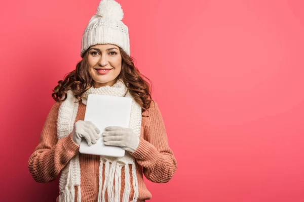 Menina sorridente em chapéu quente e cachecol segurando tablet digital no fundo rosa — Fotografia de Stock