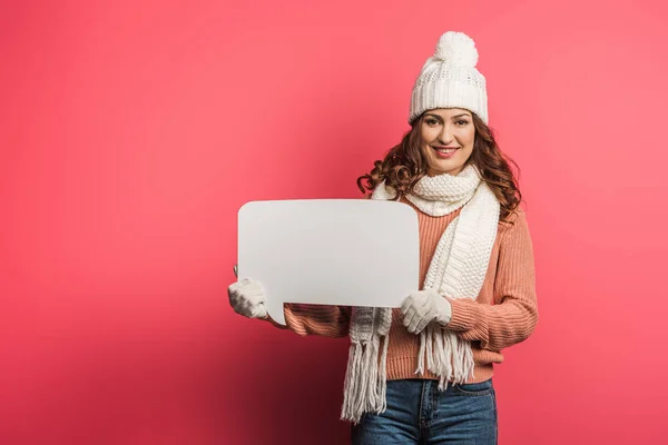 Cheerful girl in warm hat and scarf holding speech bubble on pink background — Stock Photo