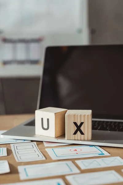 Selektiver Fokus von Holzwürfeln mit UX-Buchstaben auf Laptop mit Designer-Skizzen auf dem Tisch — Stockfoto