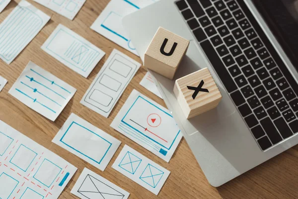 Vue grand angle des cubes avec des lettres ux sur ordinateur portable avec des esquisses de wireframe de site Web sur table en bois — Photo de stock