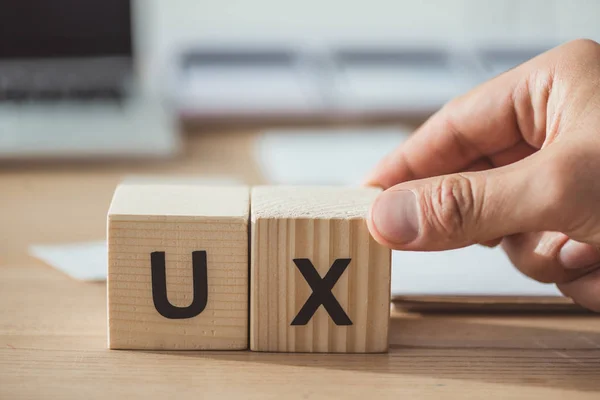 Vue recadrée de l'homme tenant un cube en bois avec des lettres ux à la table en bois — Photo de stock