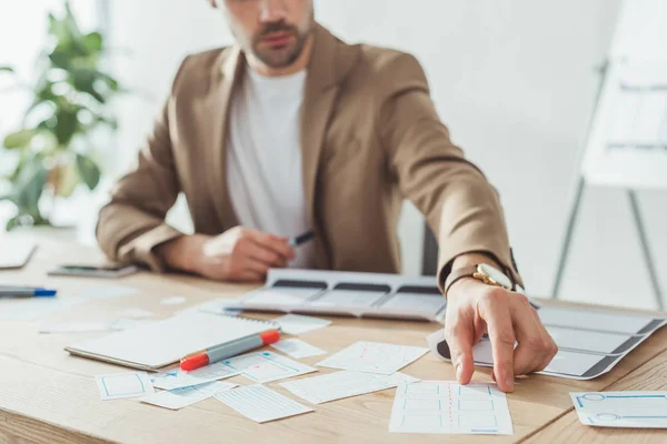 Cropped view of us designer planning applications for mobile phone at table, selective focus — Stock Photo