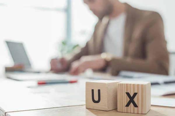 Enfoque selectivo de cubos de madera con letras ux y diseñador creativo trabajando en la mesa — Stock Photo